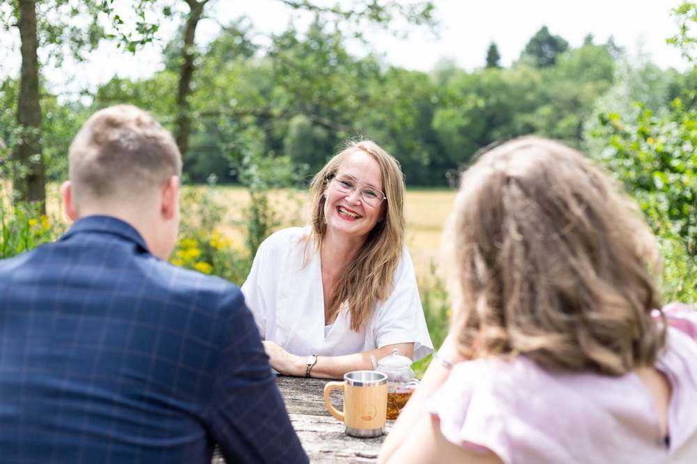 Lizette in gesprek met het bruidspaar aan de houten tafel buiten